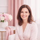 Portrait headshot of a happy woman in her 30s smiling, with a soft, warm background.